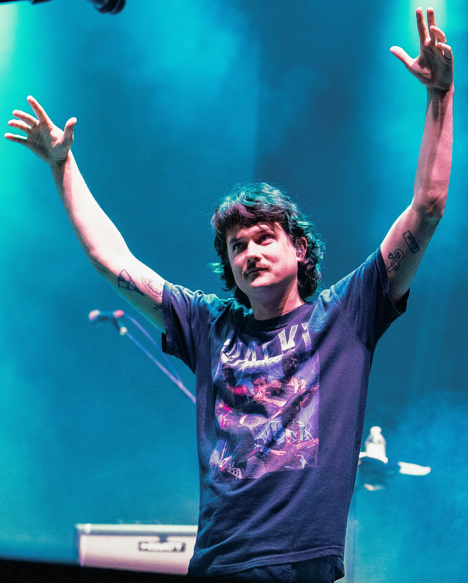Ambrose Kenny-Smith (The Murlocs, King Gizzard) walks on stage wearing a fanmade t-shirt at a King Gizzard & The Lizard Wizard concert at Boston's Stage at Suffolk Downs in August 2024