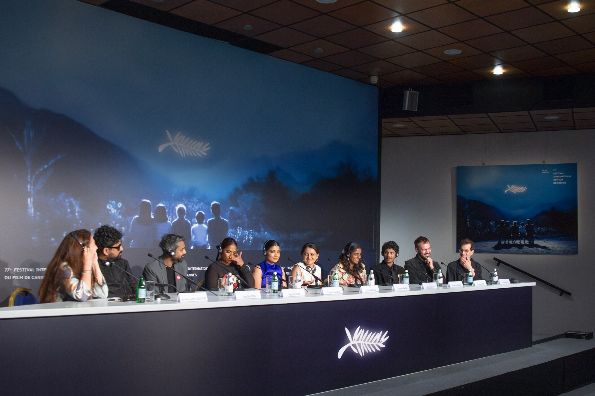 Wide shot. From left to right: Moderator Guillemette Odicino, Actresses Chhaya Kadam, Divya Prabha, director Payal Kapadia, actress Kani Kusruti, actor Hridhu Haroon, and Producers Thomas Hakim and Julien Graff at All We Imagine As Light Press Conference at 2024 Cannes Film Festival