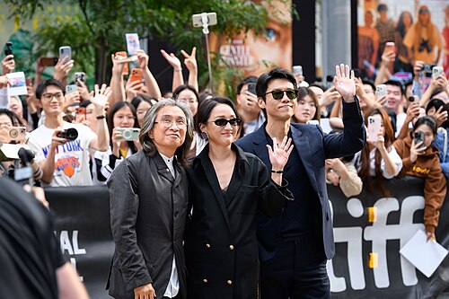 Peter Ho-sun Chan (left), Zhou Xun (middle), and Wang Xiao (right) wave to fans at the screening of The Road Not Taken at the 2026 Toronto International Film Festival.